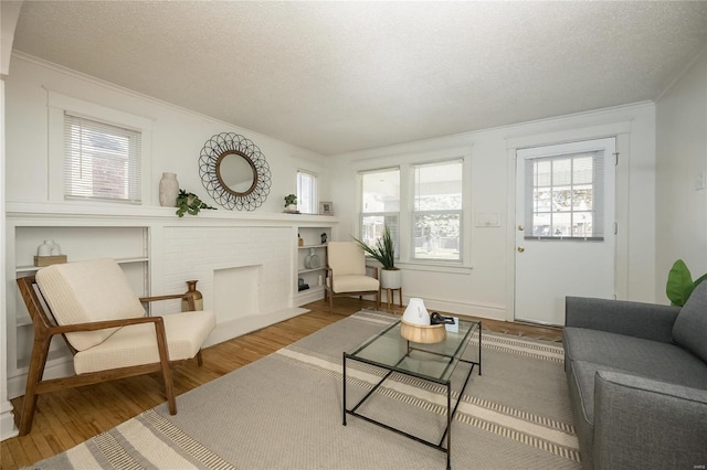 living room with a brick fireplace, ornamental molding, a textured ceiling, and hardwood / wood-style flooring