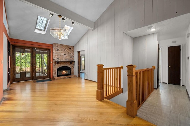 living room featuring french doors, lofted ceiling with skylight, light hardwood / wood-style floors, wooden walls, and a fireplace