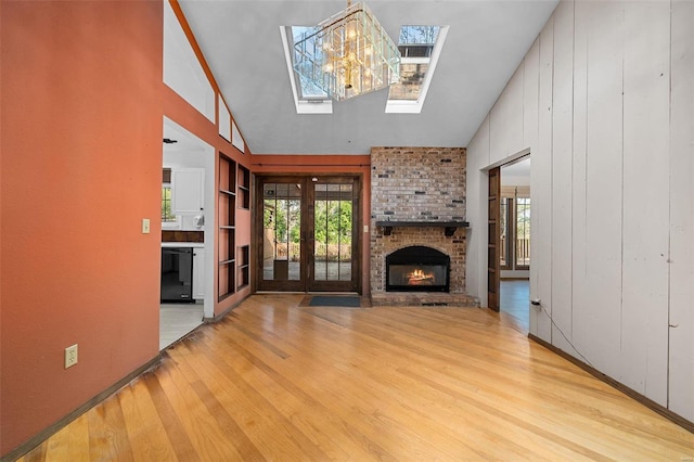 unfurnished living room featuring a skylight, french doors, a brick fireplace, wooden walls, and light wood-type flooring