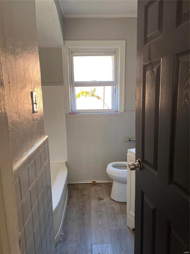 bathroom featuring radiator, a tub to relax in, toilet, tile walls, and hardwood / wood-style flooring