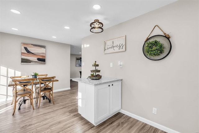 bar with light hardwood / wood-style flooring, white cabinetry, and light stone counters