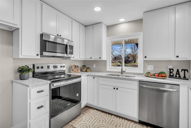 kitchen featuring light stone counters, stainless steel appliances, white cabinetry, and sink