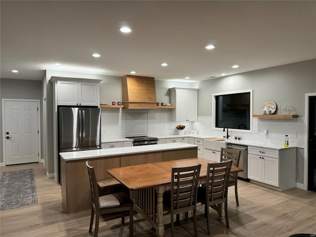 kitchen with tasteful backsplash, custom range hood, stainless steel appliances, a center island, and light hardwood / wood-style floors