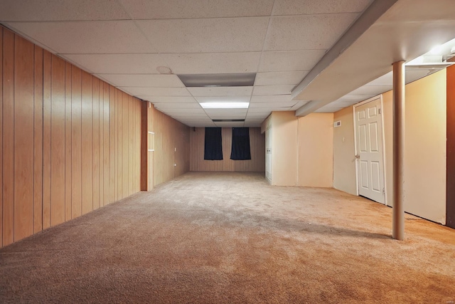 basement featuring a paneled ceiling, carpet floors, and wooden walls