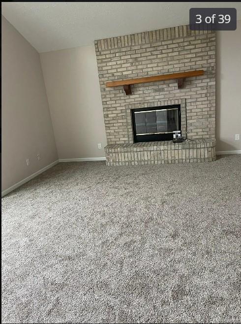 unfurnished living room featuring carpet flooring, vaulted ceiling, and a brick fireplace