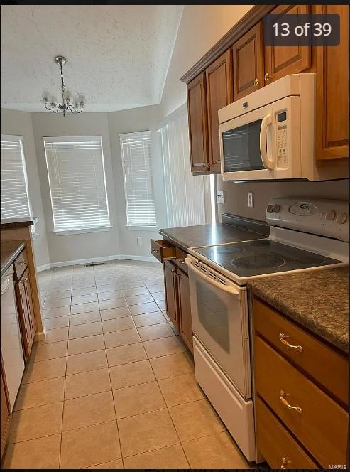 kitchen featuring white appliances, an inviting chandelier, light tile patterned floors, a textured ceiling, and decorative light fixtures