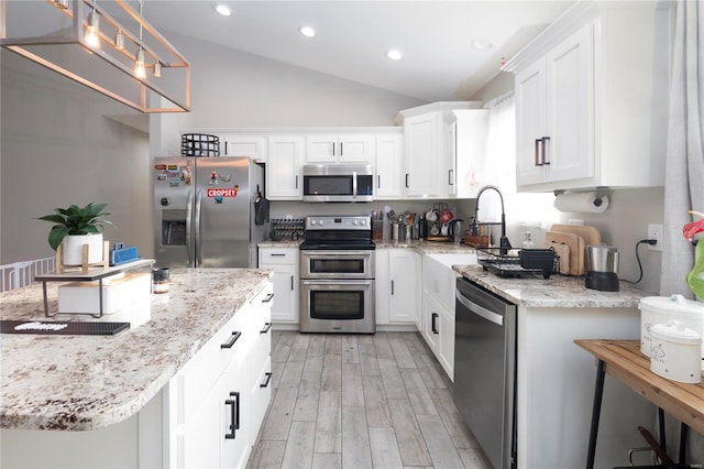 kitchen featuring white cabinetry, stainless steel appliances, a kitchen breakfast bar, light hardwood / wood-style flooring, and vaulted ceiling