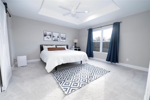 carpeted bedroom featuring a raised ceiling, a barn door, and ceiling fan