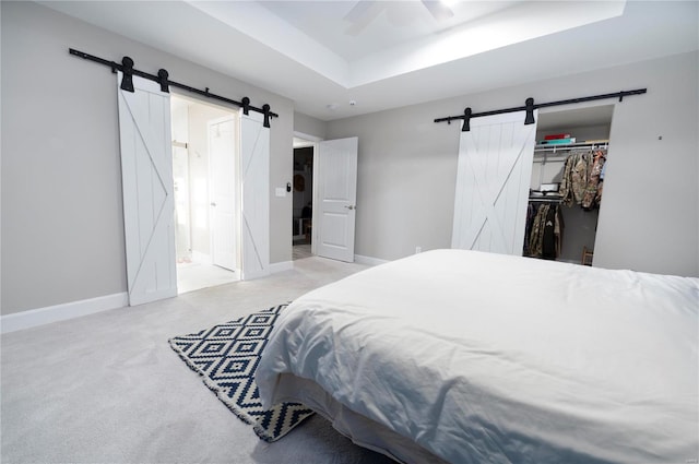 carpeted bedroom featuring ceiling fan, a raised ceiling, a barn door, ensuite bathroom, and a closet