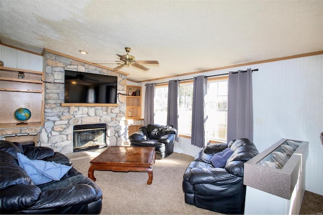 carpeted living room with ceiling fan, a stone fireplace, ornamental molding, and a textured ceiling