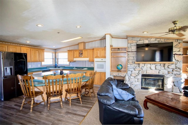 dining area featuring a textured ceiling, ceiling fan, crown molding, a fireplace, and hardwood / wood-style floors