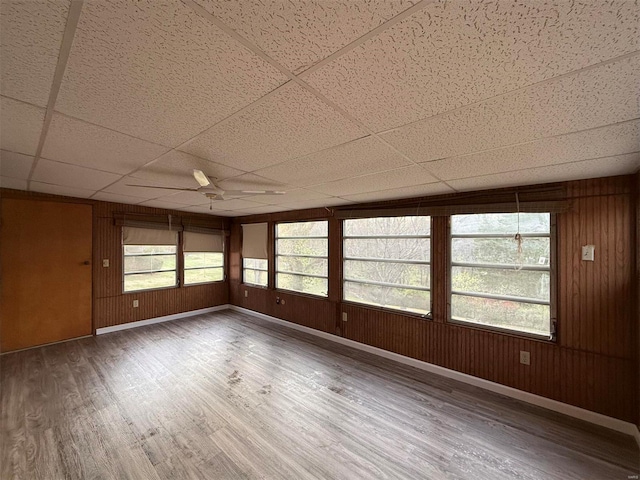 unfurnished room with hardwood / wood-style flooring, a drop ceiling, wood walls, and ceiling fan