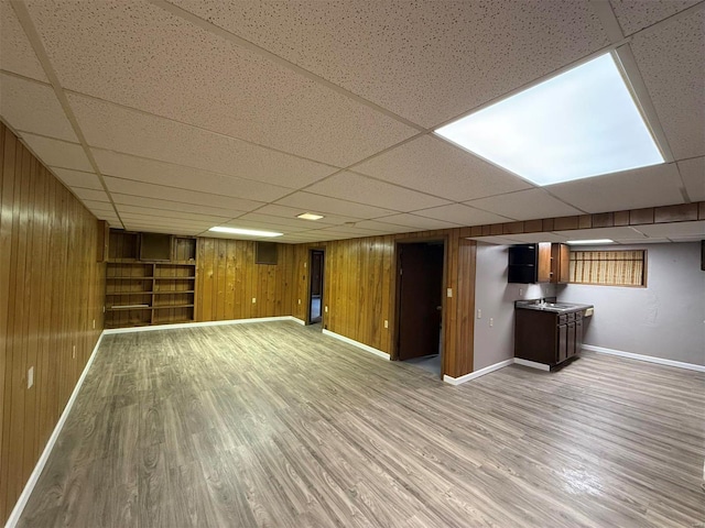 basement with a paneled ceiling, light hardwood / wood-style floors, and wood walls