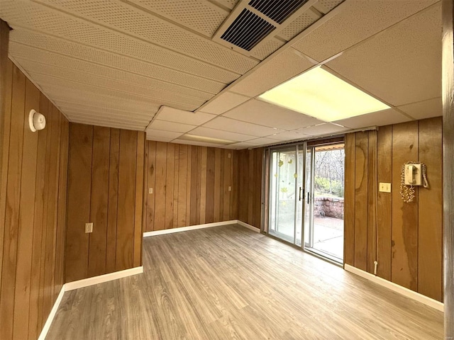 unfurnished room with hardwood / wood-style floors, a paneled ceiling, and wooden walls