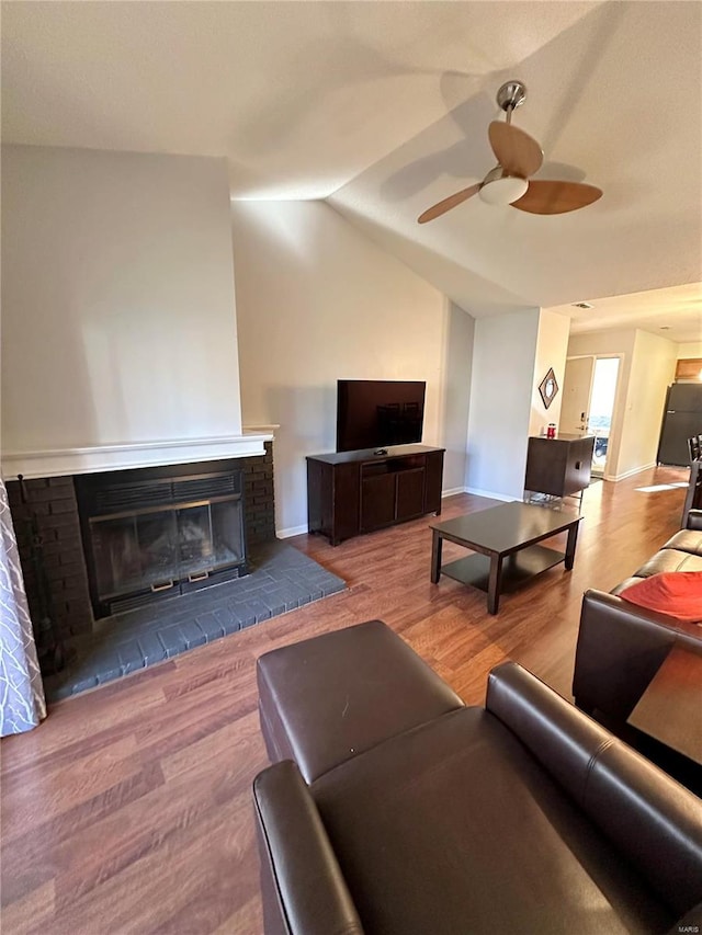 living room featuring ceiling fan, light hardwood / wood-style floors, lofted ceiling, and a brick fireplace