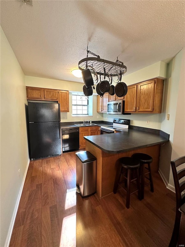 kitchen featuring sink, dark wood-type flooring, kitchen peninsula, a textured ceiling, and black appliances