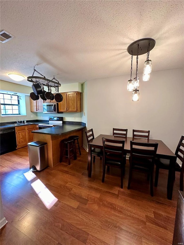 kitchen with dark wood-type flooring, black dishwasher, kitchen peninsula, decorative light fixtures, and a textured ceiling