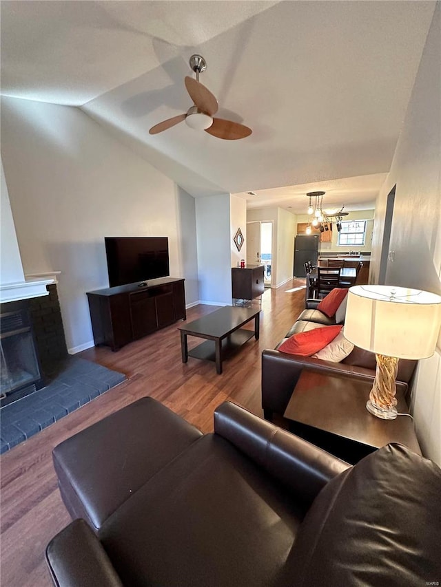 living room featuring a fireplace, ceiling fan with notable chandelier, vaulted ceiling, and hardwood / wood-style flooring