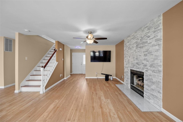 unfurnished living room with a stone fireplace, ceiling fan, and light hardwood / wood-style floors