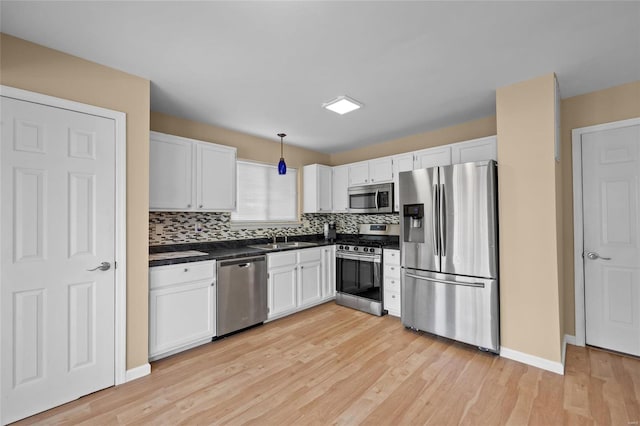 kitchen featuring sink, light hardwood / wood-style flooring, appliances with stainless steel finishes, decorative light fixtures, and white cabinetry