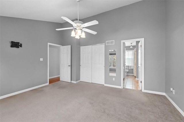 unfurnished bedroom with light carpet, a high ceiling, ensuite bath, ceiling fan, and a closet