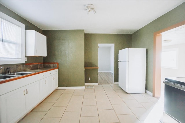 kitchen with white cabinets, white refrigerator, light tile patterned flooring, and sink