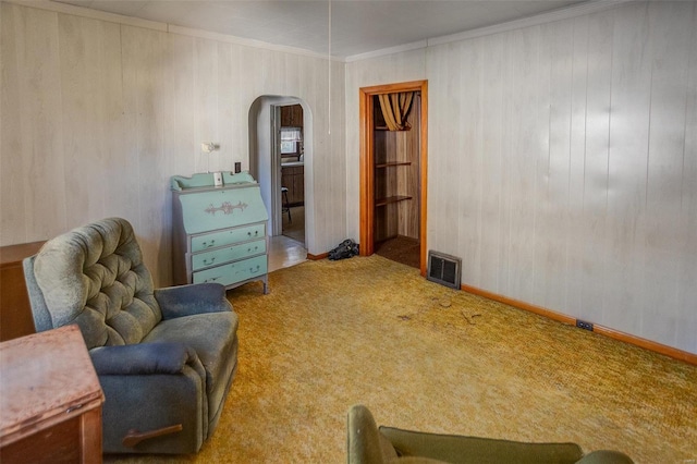 sitting room featuring carpet floors, wooden walls, and ornamental molding