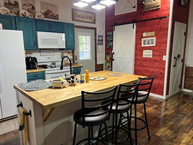 kitchen with white appliances, wooden walls, blue cabinetry, a barn door, and dark hardwood / wood-style floors