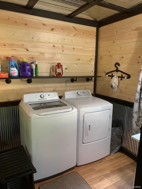 laundry room with wood walls, light wood-type flooring, and independent washer and dryer