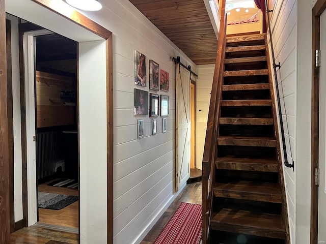 stairway featuring a barn door, wood walls, wooden ceiling, and hardwood / wood-style flooring