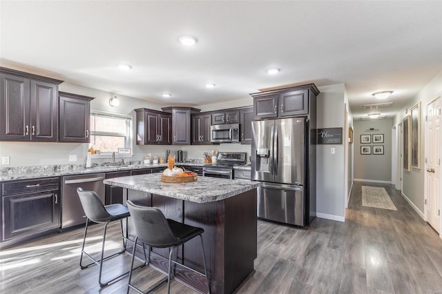 kitchen featuring a breakfast bar, dark brown cabinetry, stainless steel appliances, dark wood-type flooring, and a kitchen island