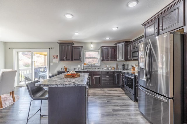 kitchen with hardwood / wood-style floors, a center island, sink, appliances with stainless steel finishes, and dark brown cabinets