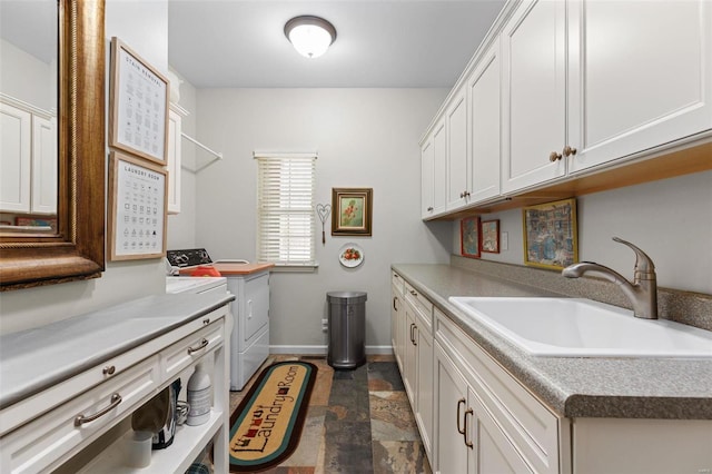 laundry area with washing machine and clothes dryer, cabinet space, stone finish floor, a sink, and baseboards