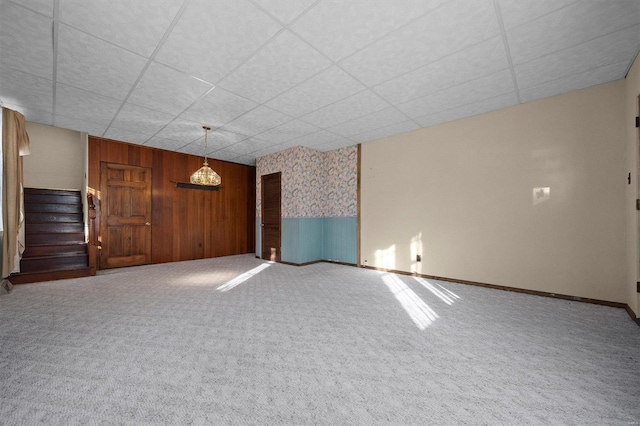 spare room with a drop ceiling, wood walls, and carpet floors