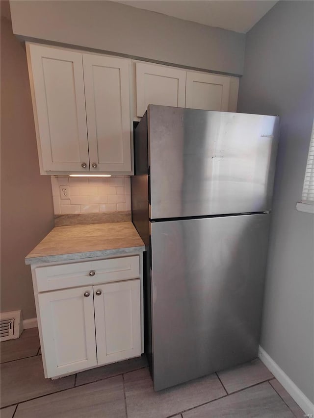 kitchen featuring decorative backsplash, stainless steel fridge, and white cabinets