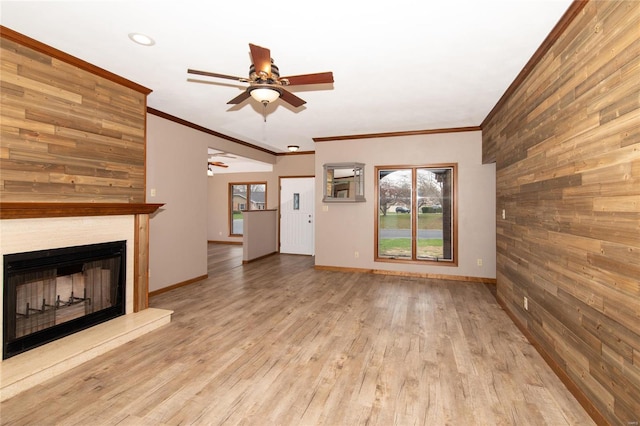 unfurnished living room with a large fireplace, wooden walls, light hardwood / wood-style flooring, and ornamental molding