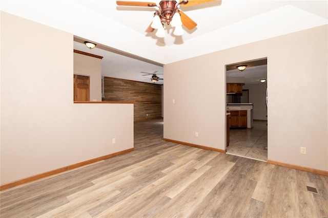 unfurnished room featuring light wood-type flooring, ceiling fan, and wood walls