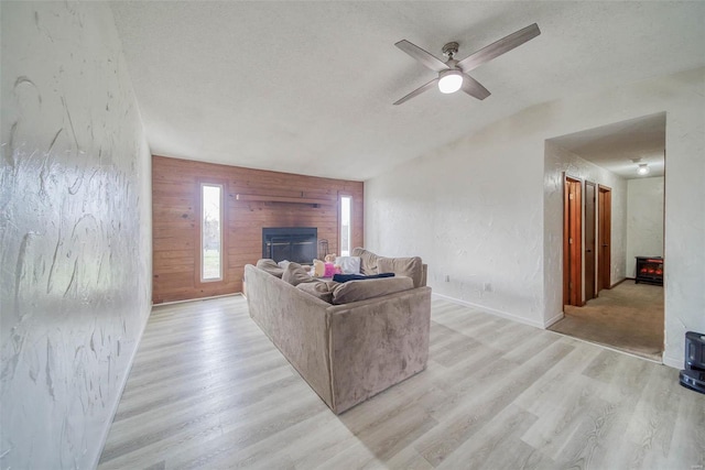 living room featuring wood walls, ceiling fan, a fireplace, a textured ceiling, and light hardwood / wood-style floors