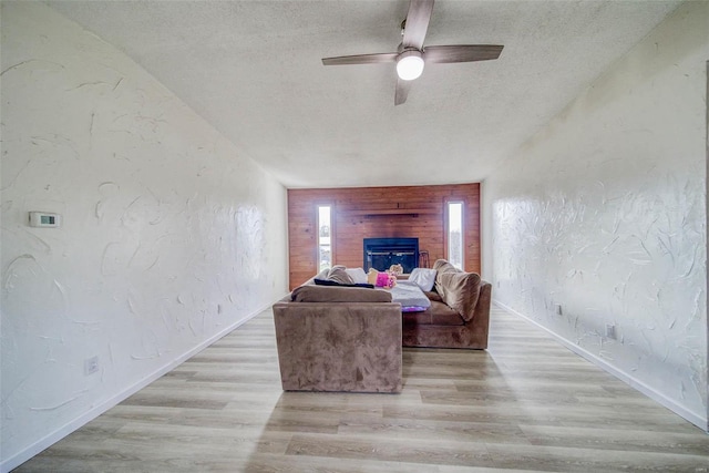 living room featuring vaulted ceiling, ceiling fan, light hardwood / wood-style flooring, and a textured ceiling