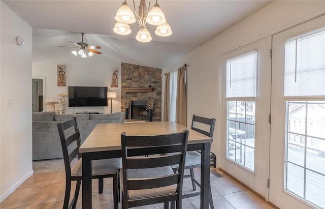 dining area with ceiling fan with notable chandelier, vaulted ceiling, a fireplace, and light tile patterned floors