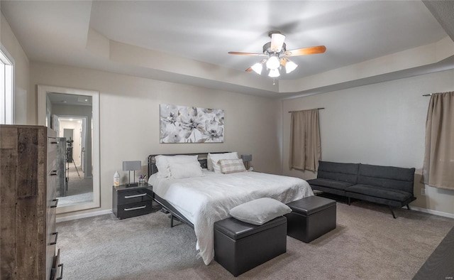 carpeted bedroom with a raised ceiling and ceiling fan