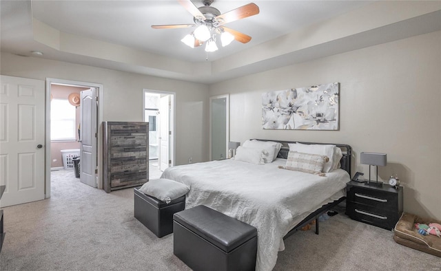 bedroom with ensuite bath, light carpet, ceiling fan, and a raised ceiling