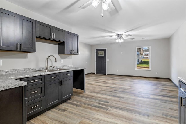 kitchen with ceiling fan, light stone counters, sink, and light hardwood / wood-style flooring