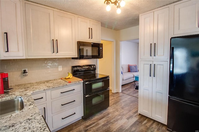 kitchen with a textured ceiling, hardwood / wood-style flooring, white cabinetry, and black appliances