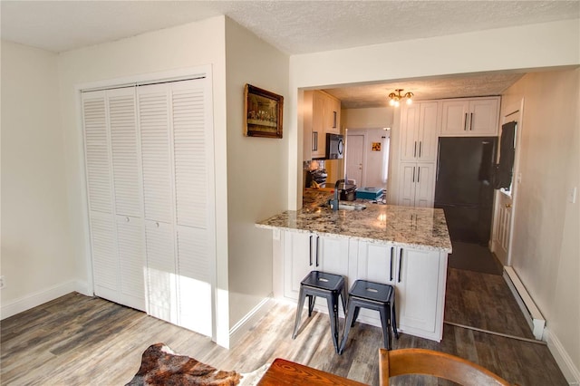 kitchen with a baseboard radiator, black fridge, kitchen peninsula, wood-type flooring, and a textured ceiling