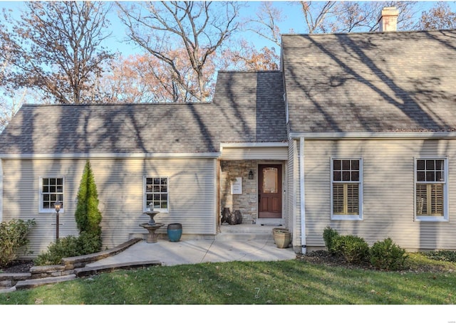 view of front facade featuring a shingled roof, a front yard, stone siding, a chimney, and a patio area