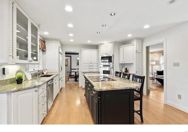 kitchen with appliances with stainless steel finishes, a kitchen bar, light wood-style flooring, and white cabinets