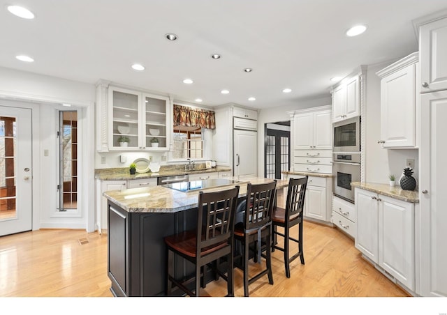 kitchen with white cabinets, a kitchen island, appliances with stainless steel finishes, a kitchen breakfast bar, and light wood-style floors