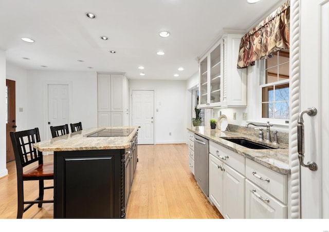 kitchen featuring light wood finished floors, a breakfast bar area, a sink, white cabinetry, and stainless steel dishwasher