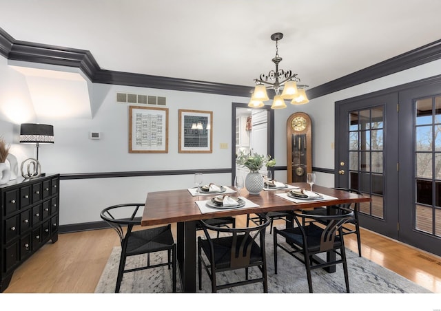 dining area with a chandelier, light wood-style flooring, visible vents, french doors, and crown molding